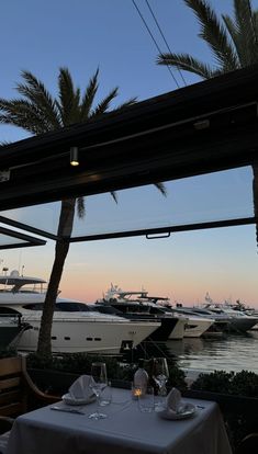 an outdoor dining area with boats in the water and palm trees on either side of it