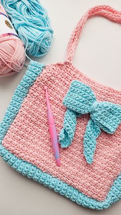 a crocheted bag with a pink and blue bow sits next to some yarn