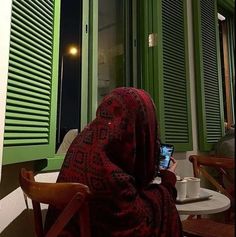 a woman in a red shawl sitting at a table with a laptop computer on it