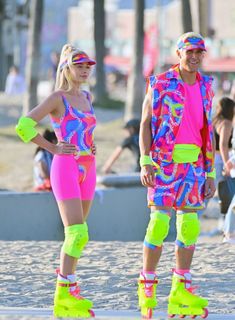 two people dressed in neon colored clothing and roller skates on the beach with palm trees behind them