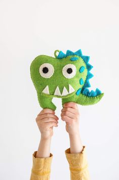 a child holding up a green stuffed animal with big eyes and teeth on it's face