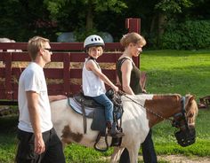 two young children riding on the back of a brown and white horse next to a woman