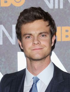 a close up of a person wearing a suit and tie with a smile on his face