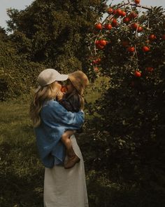 a woman holding a child while standing in front of an apple tree