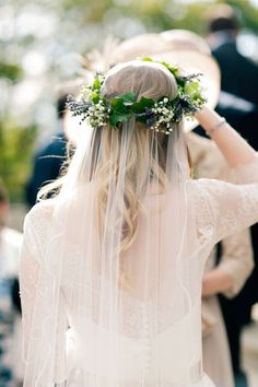 a woman wearing a veil with flowers in her hair is walking down the aisle at a wedding