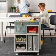 a young boy sitting on top of a kitchen counter next to a woman in a white shirt