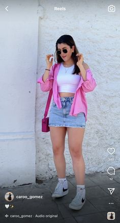 a woman standing in front of a white wall wearing shorts and a pink cardigan