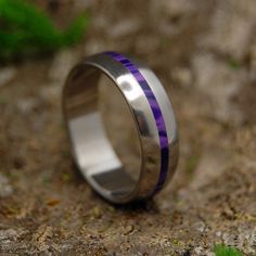 a wedding ring with purple and silver inlays sits on the ground next to some grass