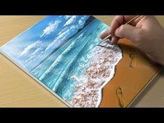 a person is drawing on a piece of paper with water and clouds in the background