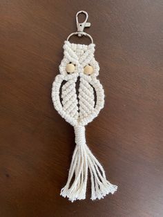 an owl keychain made out of white yarn on top of a wooden table