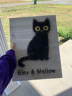 a person holding up a wooden sign with a black cat on it's face