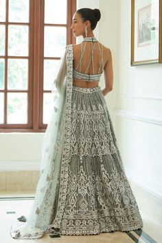 Charcoal grey net lehenga embroidered with silver leather applique, overlaid with zari, silver beadwork, sequins and crystals and attached cancan. Paired with a halter neck cutout padded choli with bead and zari work and dupatta.
Components: 3
Pattern: Embroidered
Type Of Work: Sequin, Bead, Crystal
Neckline: Halter
Sleeve Type: Sleeveless
Fabric: Net, Satin
Color: Grey
Other Details: 
Attached cancan
Padded Blouse
Approx. product weight: 7 - 9 kgs
Lehenga length: 45 inches
Occasion: Wedding, Br Silver Cutdana Lehenga For Wedding, Silver Party Choli With Cutdana Details, Designer Embellished Silver Lehenga, Elegant Silver Lehenga With Cutdana Detail, Glamorous Embellished Silver Lehenga, Sequin Halter, Net Lehenga, Bridal Lehenga Red, Indian Wedding Wear