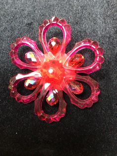 a pink flower brooch sitting on top of a black surface