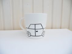 a white coffee cup with a car drawn on the side sitting on top of a table