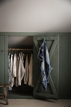 an open closet with clothes hanging on hangers and a wooden bench in front of it