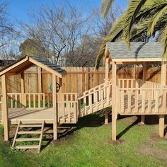 a wooden play set in the grass next to a tree and fenced in area