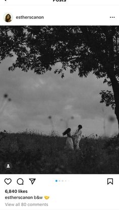 two people walking through a field under a tree