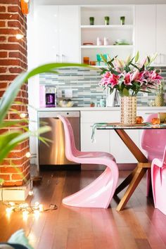 a pink table and chairs in a room with brick walls, wood flooring and white cabinets