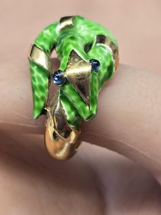 Gorgeous Trifari snake ring a done on brilliant gold plated metal.   The sake is enameled a Mottled green with a gold diamond on his head and bands of gold on his body.  Sapphire blue cabochon eyes and the band itself is gold.  There is an expansion ring I side the band and it can go anywhere from a size five to six and a half!  Pristine condition and looks fabulous on.  The snake measuring 1 1/8" by 1/2".  ABSOLUTELY ICONIC GARDEN OF EDEN! Formal Green Enamel Jewelry, Green Enamel Ring For Anniversary, Unique Green Enamel Ring For Anniversary, Unique Green Enamel Anniversary Ring, Green Snake Ring Gift, Green Snake Ring For Gift, Unique Green Snake-shaped Jewelry, Unique Green Metal Ring, Gold Snake Ring Collectible Unique Style