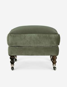 the footstool is made out of wood and green velvet, with wheels on each side