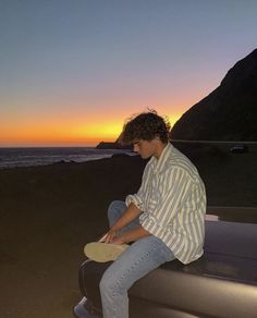 a young man sitting on the back of a pick up truck next to the ocean