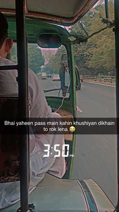 a man driving a green truck down a street next to a lush green hillside covered with trees