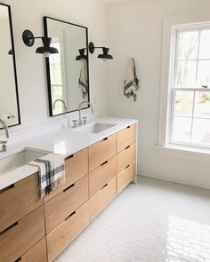 a bathroom with two sinks and mirrors on the wall next to each other in front of a window