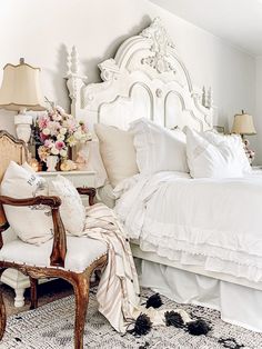 a white bed sitting in a bedroom next to a table with flowers on top of it