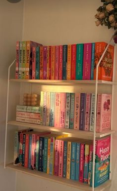 a book shelf filled with lots of books on top of a white wall next to a potted plant