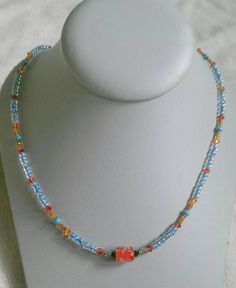 Red/orange bicone crystal beads, blue seed beads, brown seed beads, and a speckled red glass bead in the middle. Toggle clasp. Measures 19.5 inches long end to end. Orange Glass Beaded Necklace With Colorful Beads, Adjustable Orange Beaded Necklaces With Heart Beads, Adjustable Orange Beaded Necklace With Heart Beads, Orange Beaded Necklaces With Czech Glass, Orange Czech Glass Beaded Necklaces, Orange Czech Glass Beaded Necklace, Crystal Beaded Necklace, Crystal Bead Necklace, Toggle Clasp