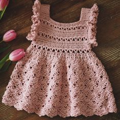 a pink crocheted dress sitting on top of a wooden table next to tulips