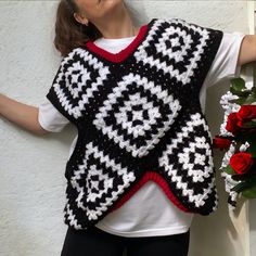 a woman wearing a black and white crochet vest with red roses in the background