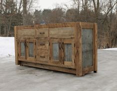 a large wooden cabinet sitting on top of a snow covered ground with trees in the background