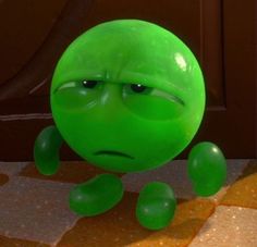 a green ball with an angry look on it's face sitting on the ground