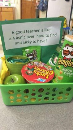 a green plastic basket filled with lots of food and candy next to a sign that says, a good teacher is like a 4 leaf clover, hard to find and lucky to have