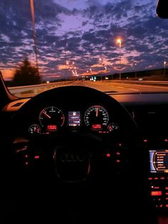 the dashboard of a car at night with clouds in the sky and street lights behind it