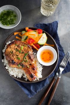 a plate with meat, rice and veggies next to a glass of water