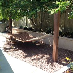 an empty hammock in the middle of a backyard area with gravel and trees