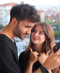 a man and woman standing next to each other looking at something on their cell phone