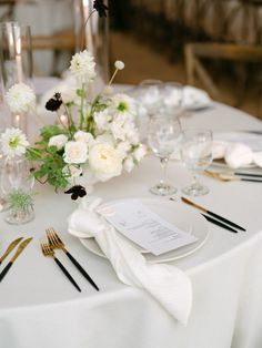 the table is set with silverware and white flowers