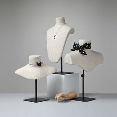 three white mannequins with black bows and hats on stands in front of a gray background