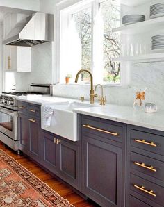 a kitchen with marble counter tops and gray cabinets, gold pulls on the faucets