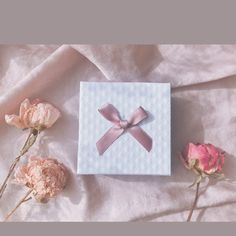 a white box with a pink bow on top of it next to some pink flowers