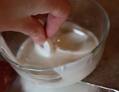 a person dipping something into a glass bowl with milk in it on a counter top