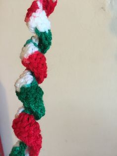 a crocheted red, white and green garland hanging from a hook on a wall