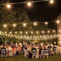 an outdoor wedding reception with string lights and white tablecloths on the lawn at night