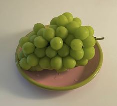 a green plate with grapes on it sitting on a white counter top next to a pink bowl