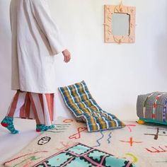 a woman in a white coat is standing on the floor next to pillows and rugs