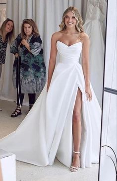 a woman standing in front of a mirror wearing a white dress with high slits