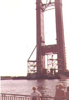 three people are standing near the water by a bridge